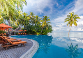 Outdoor tourism landscape. Luxurious beach resort with swimming pool and beach chairs or loungers under umbrellas with palm trees and blue sky. Summer travel and vacation background concept